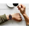 A person's hand wearing an Apple Watch is shown while holding a cup of coffee. Produktbild-Vorschau