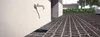 A close-up view of a dripping faucet mounted on a textured wall, with a dark brick-like pavement in the foreground and a drain grate. Produktbild-Vorschau