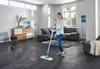 A woman is mopping a floor in a modern living room. Produktbild-Vorschau