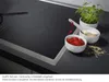 A close-up view of a modern induction cooktop with decorative elements like bowls of food and a plant. Produktbild-Vorschau