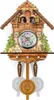 A cuckoo clock with carved wooden details, including figures in a balcony, trees, and a woodcutter. Náhled obrázku produktu