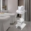 A white beauty trolley with a device on top, in a spa-like room with massage beds and a bathtub in the background. Podgląd zdjęcia produktu