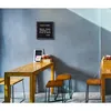 A menu board hangs on a wall above a wooden table with chairs in a cafe or restaurant setting. Produktbild-Vorschau