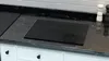 A black glass cutting board is placed on a black granite countertop in a kitchen. Anteprima dell’immagine prodotto