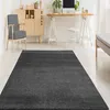 A dark gray rug is placed in a modern living room setting with a chair, a cabinet, and a desk with a computer. Produktbild-Vorschau