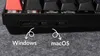 Close-up of the bottom edge of a black mechanical keyboard, showing connection ports and switchable labels for Windows and macOS operating systems. Produktbild-Vorschau