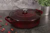 A burgundy cast iron braadpan with a silver lid handle sits on a dark gray countertop, with a potted plant in the background. Produktbild-Vorschau