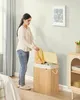 A woman is putting clothes into a laundry basket in a bedroom.