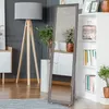 A tall, narrow mirror with a decorative frame stands in a modern living room next to a white bookshelf and a floor lamp. Náhľad obrázku produktu