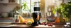 A smoothie blender is set up on a kitchen counter with various fruits and berries arranged around it. Podgląd zdjęcia produktu