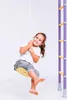 A young girl is happily swinging on a yellow disc swing attached to a rope, next to a purple climbing frame. Náhled obrázku produktu