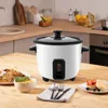 A white rice cooker is placed on a wooden table, with plates of food and cutlery around it, in a kitchen setting. Produktbild-Vorschau