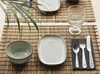 A table setting with plates, a bowl, cutlery, and a glass on a bamboo placemat. Produktbild-Vorschau