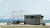 A portable power station and a drone are placed on a concrete surface with a body of water and industrial structures in the background. Náhled obrázku produktu