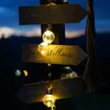 A wooden signpost with directional arrows pointing to different areas, decorated with string lights. Produktbild-Vorschau