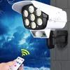 Weiße Solar-Sicherheitsleuchte mit mehreren LED-Lampen und einem Bewegungssensor, montiert an einer Wand, mit einer Hand, die eine Fernbedienung hält Voir les images du produit
