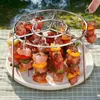 A metal grill rack with skewers of food, including meat and vegetables, being cooked outdoors. Náhľad obrázku produktu