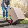A person is using a hand truck to move a large cardboard box up a set of outdoor stairs. Náhled obrázku produktu