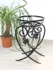 A black metal plant stand with decorative leaf motifs is shown next to a potted plant. Náhled obrázku produktu
