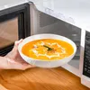 A hand is placing a bowl of soup into a microwave. Náhled obrázku produktu