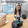 A person's hand is holding a coffee cup next to a 5-in-1 phone speaker stand with a phone on it. Produktbild-Vorschau