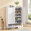 A white shoe cabinet with multiple shelves filled with shoes, placed in a room with a window and an umbrella stand. Náhľad obrázku produktu