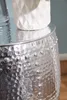 A close-up of a silver hammered metal side table with a white textured vase on top. Náhled obrázku produktu