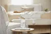 A candle is placed on a small table in front of a bed in a bedroom. Produktbild-Vorschau