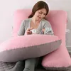 A woman is holding a baby while sitting on a bed with a large J-shaped pillow. Náhled obrázku produktu