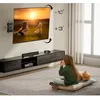 A child sits on the floor watching a TV mounted on the wall, which is displaying a picture of two children and a teddy bear. Produktbild-Vorschau
