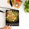 A top-down view of a person's hand adjusting the settings on an induction cooktop while vegetables are being stir-fried in a pan. Voir les images du produit