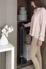 A woman is standing next to a tall, black tower fan in a closet. Produktbild-Vorschau