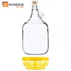 A clear glass jug with a handle and a gold cap, and a yellow basket below it, on a white background. Voir les images du produit