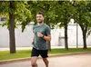 A man is jogging in a park with trees and a wall in the background. Náhled obrázku produktu