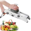 A person is using a white mandoline slicer with a basket of fresh vegetables and jars of pickles in the foreground. Produktbild-Vorschau