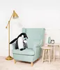 A plush penguin with its baby sits on a mint green armchair next to a floor lamp and small side tables. Podgląd zdjęcia produktu