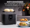A black toaster with a bun warmer is shown on a kitchen counter, with croissants and a sandwich in the foreground. Produktbild-Vorschau