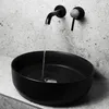 A close-up view of a black ceramic vessel sink with water running from a wall-mounted faucet. Náhled obrázku produktu