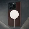 A dark brown leather wallet case for an iPhone 16 Pro is shown with a white MagSafe charger attached. Anteprima dell’immagine prodotto