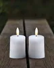 Two white LED candles with flickering flames sit on a wooden surface, with a blurred green background. Produktbild-Vorschau