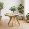 A round wooden dining table set for a meal, with plants in the background. Voir les images du produit