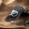 A black iPhone case with a white MagSafe ring is partially buried in sand, with some debris in the background. Produktbild-Vorschau