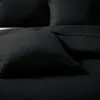 A close-up view of a black quilted blanket or bedspread with a geometric triangle pattern. Produktbild-Vorschau