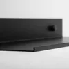 A close-up, side view of a black metal shelf mounted on a white wall. Náhľad obrázku produktu
