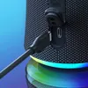 Close-up of a black Bluetooth speaker with a USB-C cable being plugged into it. The speaker has a textured fabric surface and a colorful LED light ring at the bottom. Produktbild-Vorschau