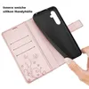 A hand is holding a black phone case, which is being inserted into a rose gold flip case with card slots and a floral design. Produktbild-Vorschau