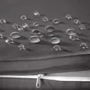 Close-up of water droplets on a gray fabric surface, with a zipper visible in the foreground. Produktbild-Vorschau