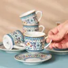 A hand is holding a coffee cup from a set of ornate coffee cups and saucers. Produktbild-Vorschau