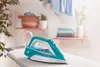 An iron is placed on an ironing board in a laundry room setting, with shelves holding folded clothes and a basket in the background. Produktbild-Vorschau