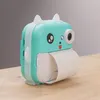 A teal and white toy camera printer with a roll of paper coming out of it, sitting on a wooden surface. Náhľad obrázku produktu